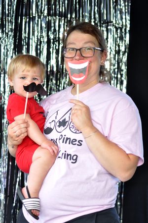 People posing with fun paper mustache and smile props against a silver tinsel backdrop.