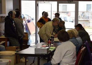 People line up at tables in an indoor space to receive food or supplies.