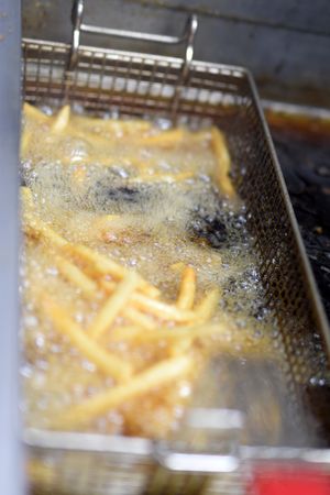 Close-up of french fries being deep fried in hot oil with bubbles forming around them.