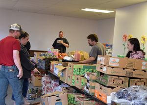 Volunteers organize and sort food items on tables at what appears to be a food bank or donation center.