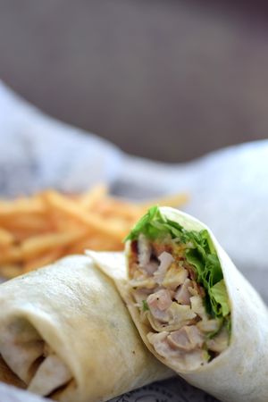 Fresh chicken wraps with lettuce and fillings arranged in a row on a light surface.