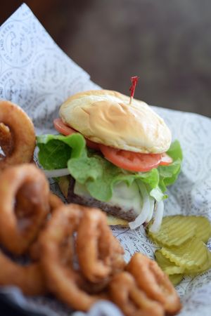 Juicy hamburger with lettuce and tomato served alongside crispy onion rings.