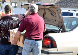 People gather outside near parked cars during what appears to be a community distribution event.