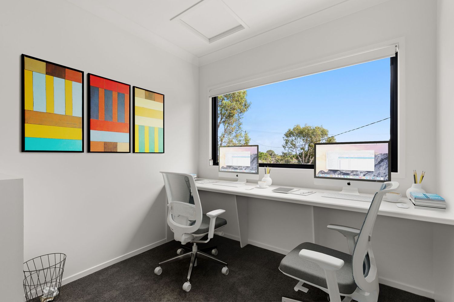 Contemporary home office with dual monitors, white desks, ergonomic chairs, and colorful wall art.