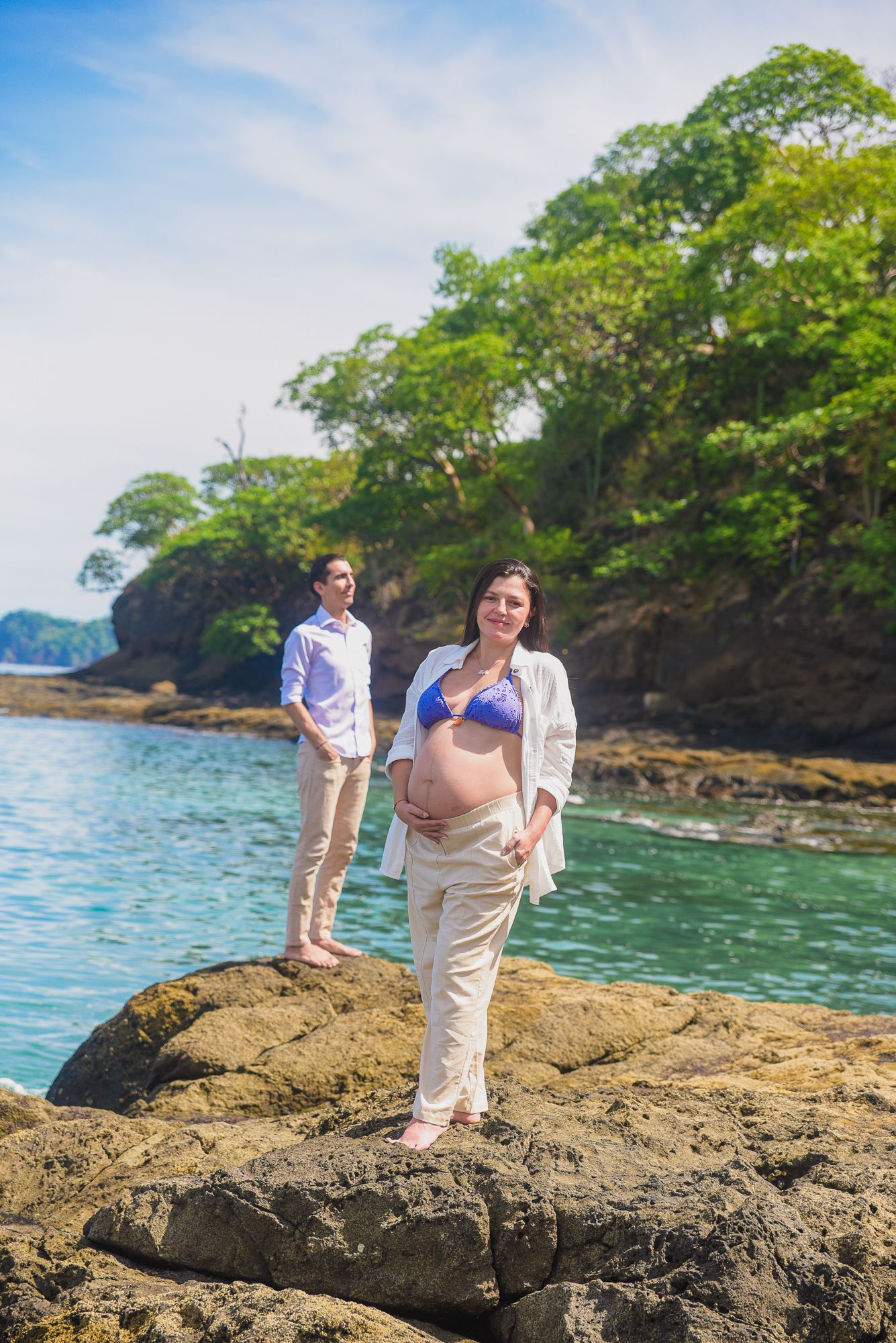 A couple strolls along a scenic rocky beach with blue ocean waves and coastal cliffs in the background.