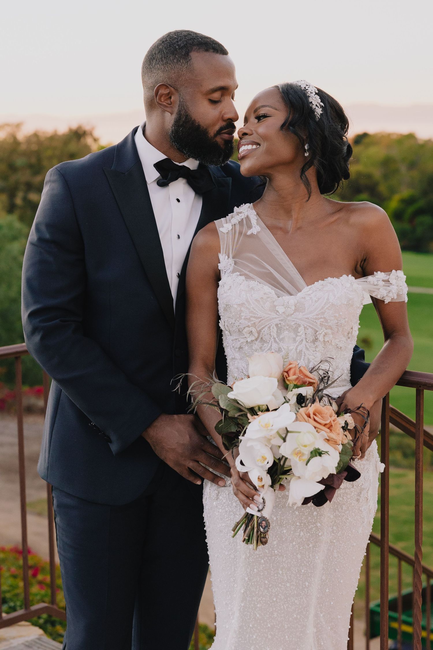 Elegant bride and groom share an intimate moment on a balcony at golden hour sunset.