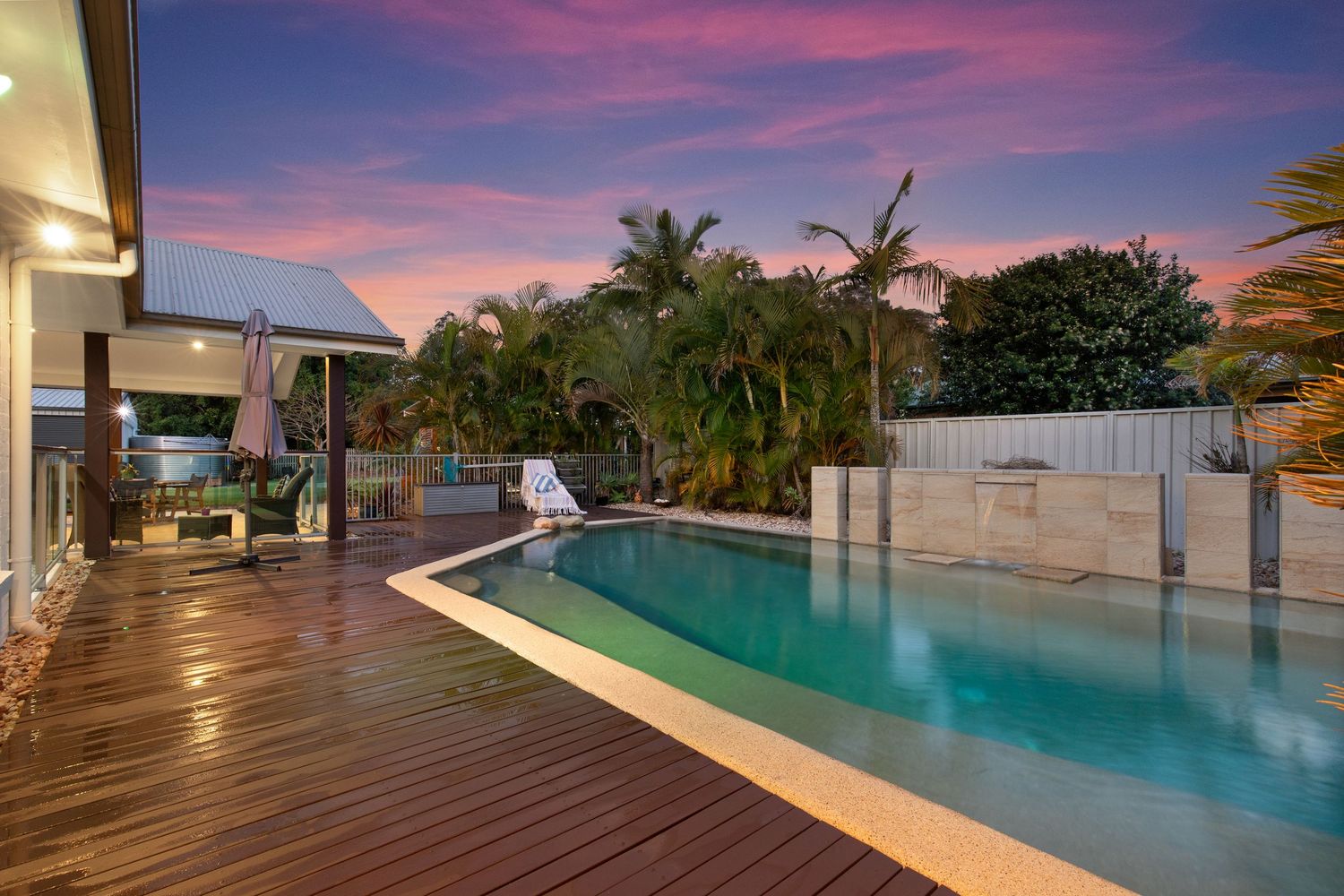 Resort-style pool with timber decking, sun loungers and tropical palms photographed at vibrant sunset.