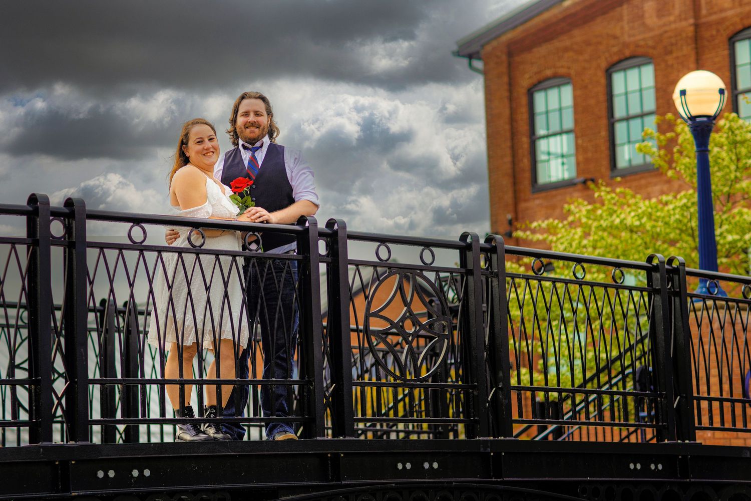 A couple poses on a wrought iron balcony with dramatic storm clouds in the background at sunset.