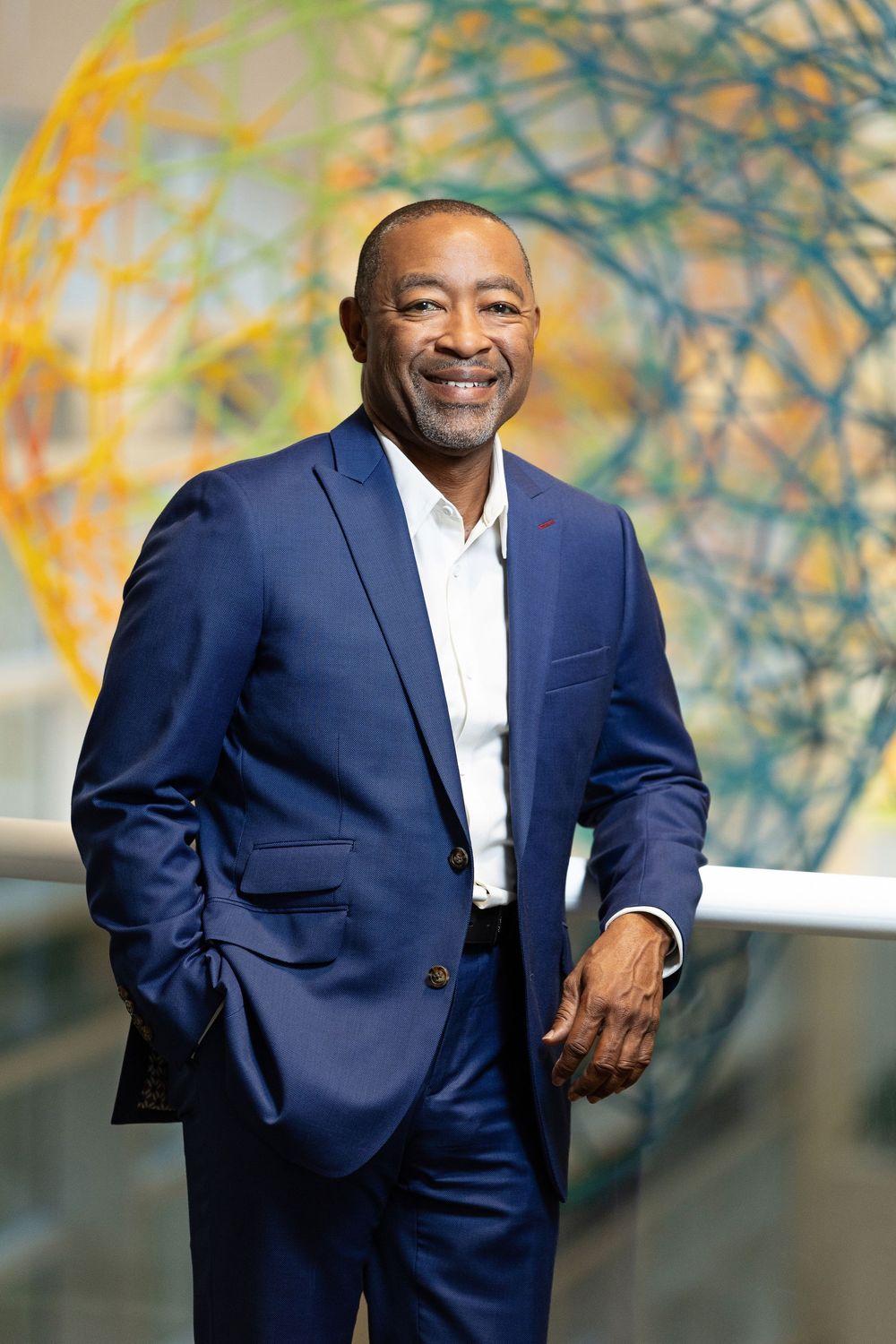 Professional in navy suit posing against artistic backdrop with warm lighting.
