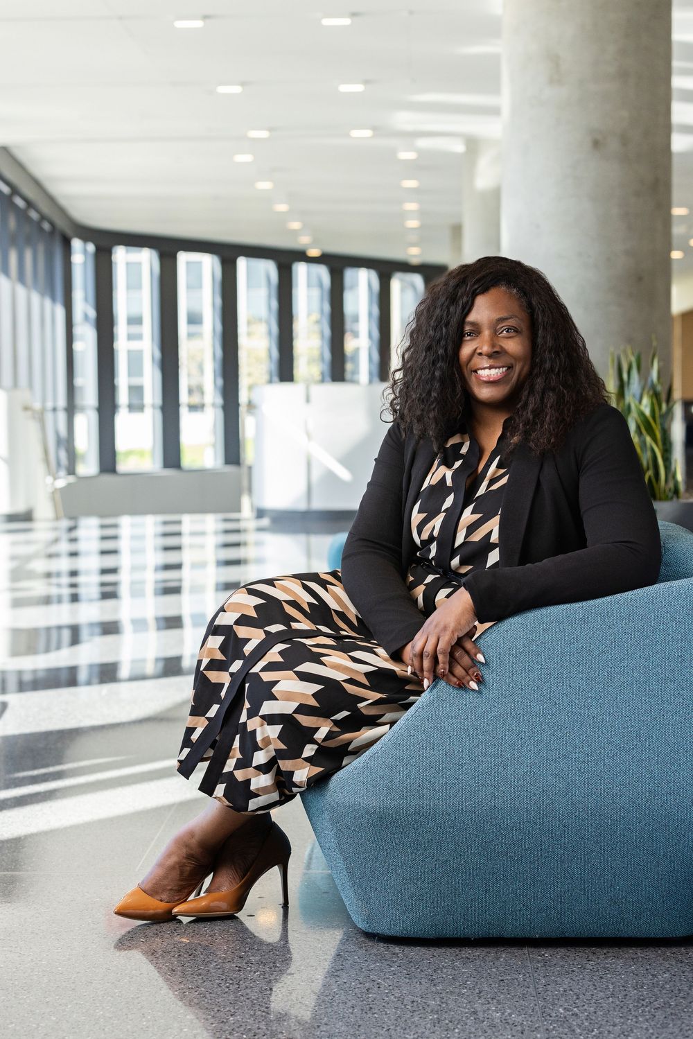 Professional in black blazer and patterned dress lounging on blue office furniture.