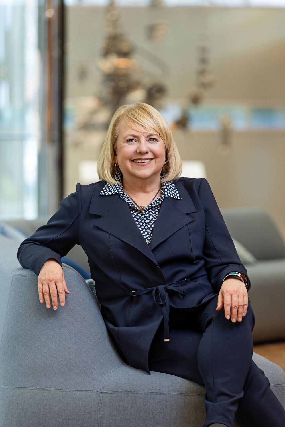 Professional in navy blazer relaxing on grey office couch.
