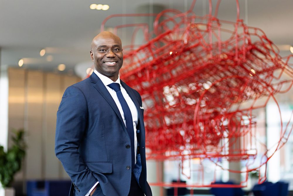 Professional in navy suit stands in modern office with striking red art installation.