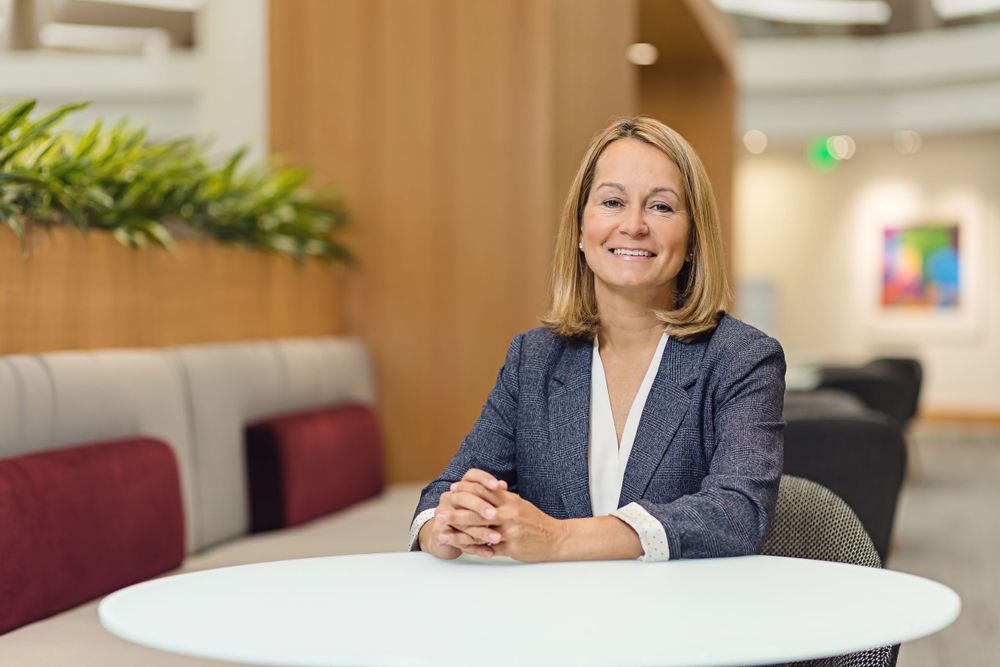 Professional in business attire sits at white table in modern office environment.