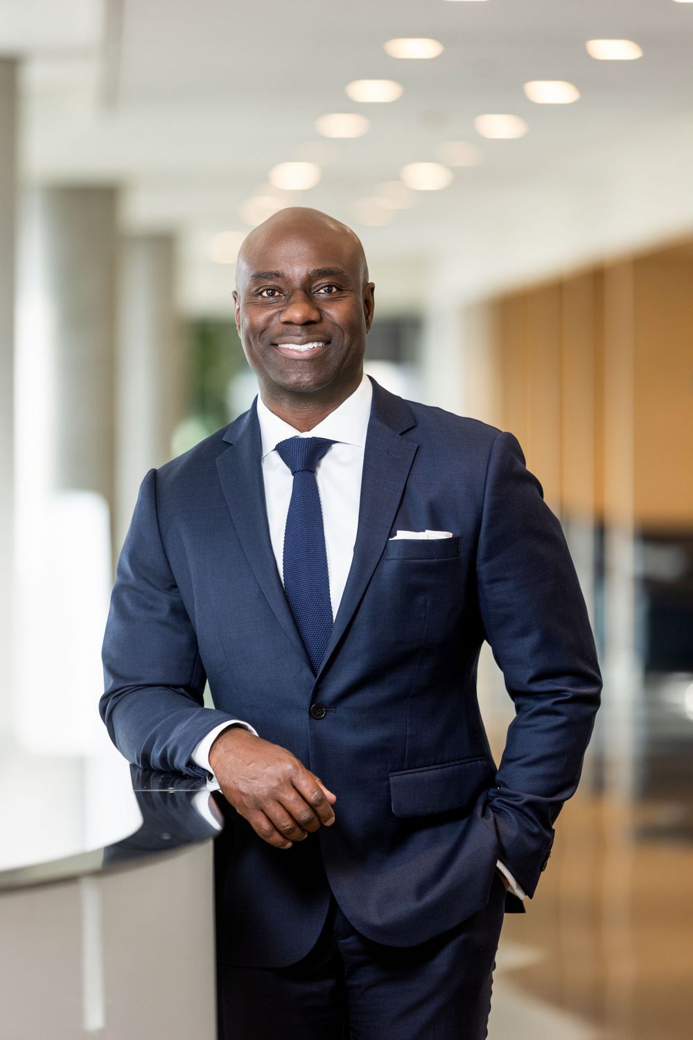 Professional in dark navy suit standing in modern office hallway.