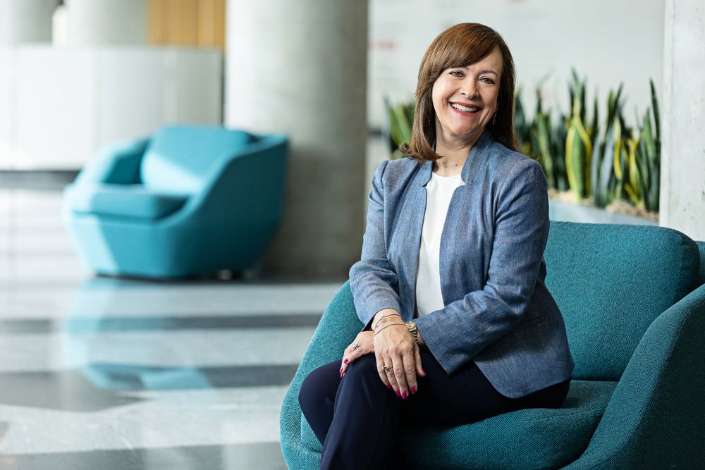 Professional in business attire sits on a turquoise chair in modern office lobby.