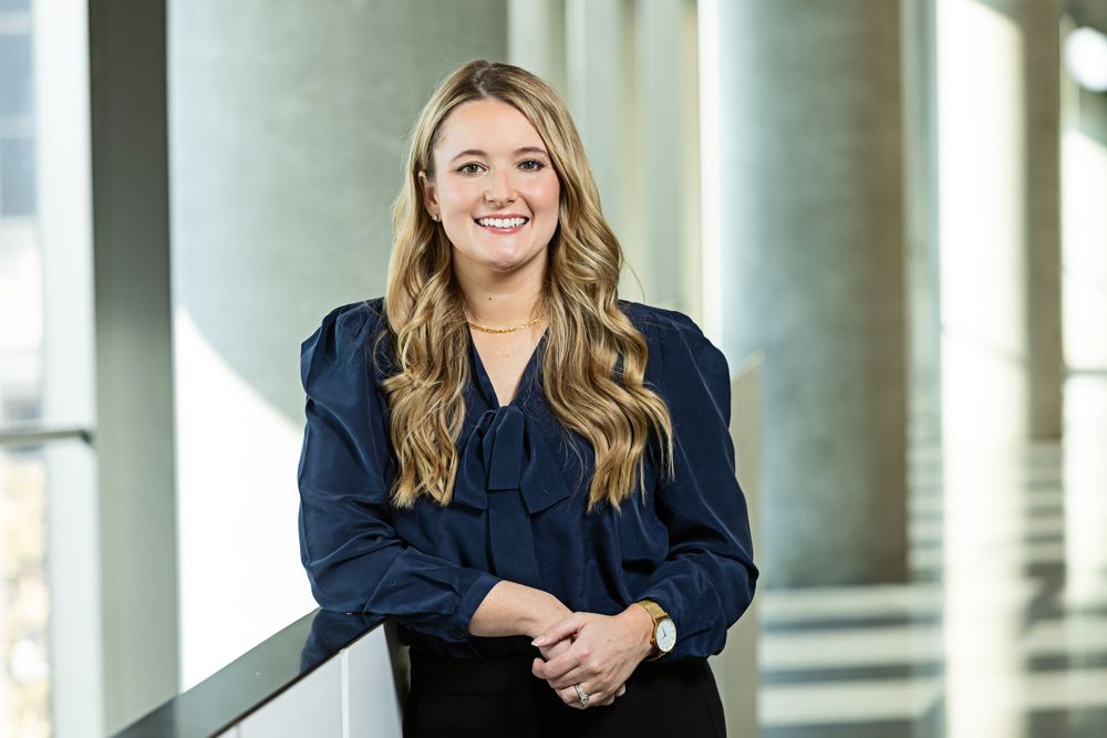 Professional in navy blazer poses in modern office setting with columns.