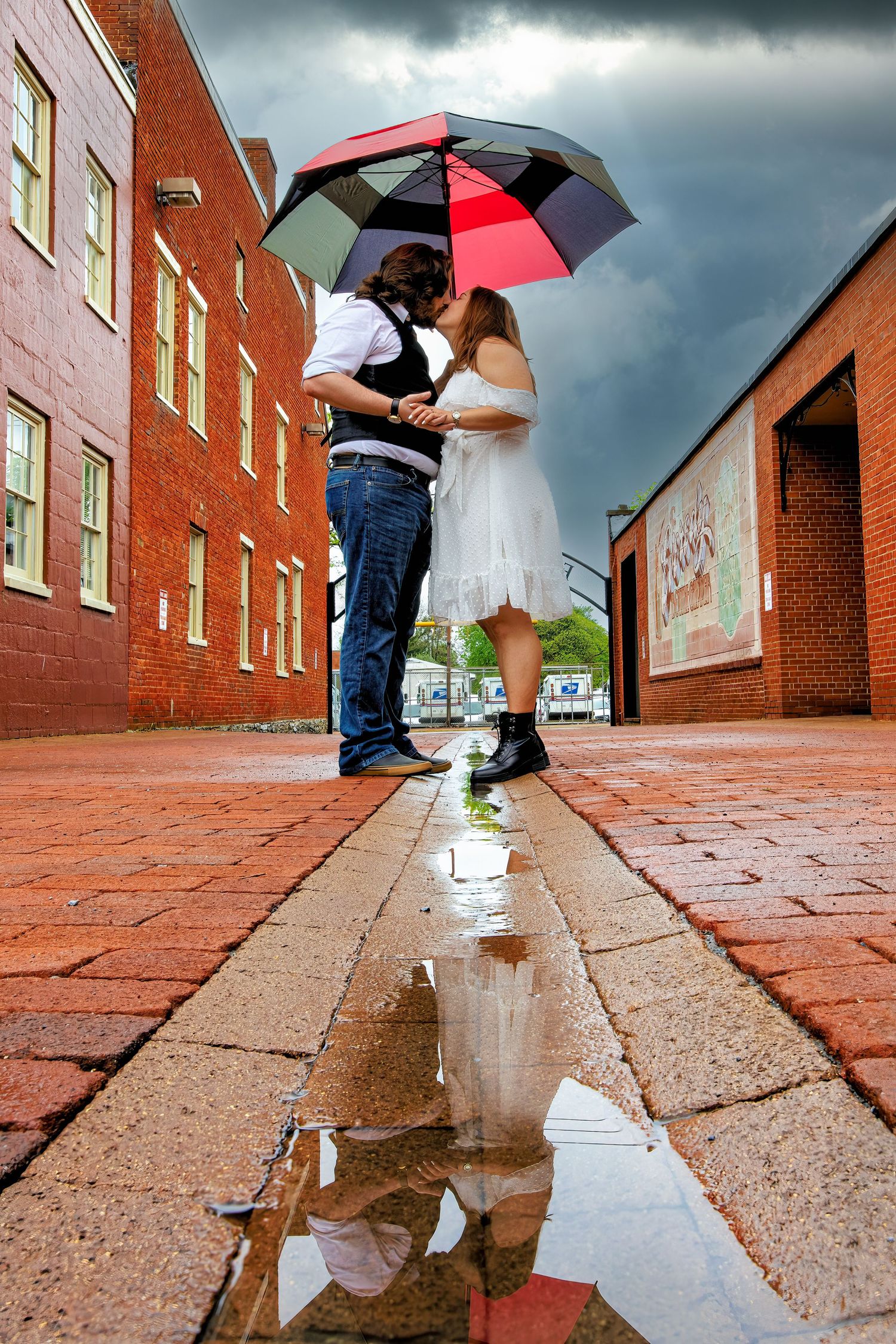 A couple walks together on a brick pathway next to a red brick building wall.