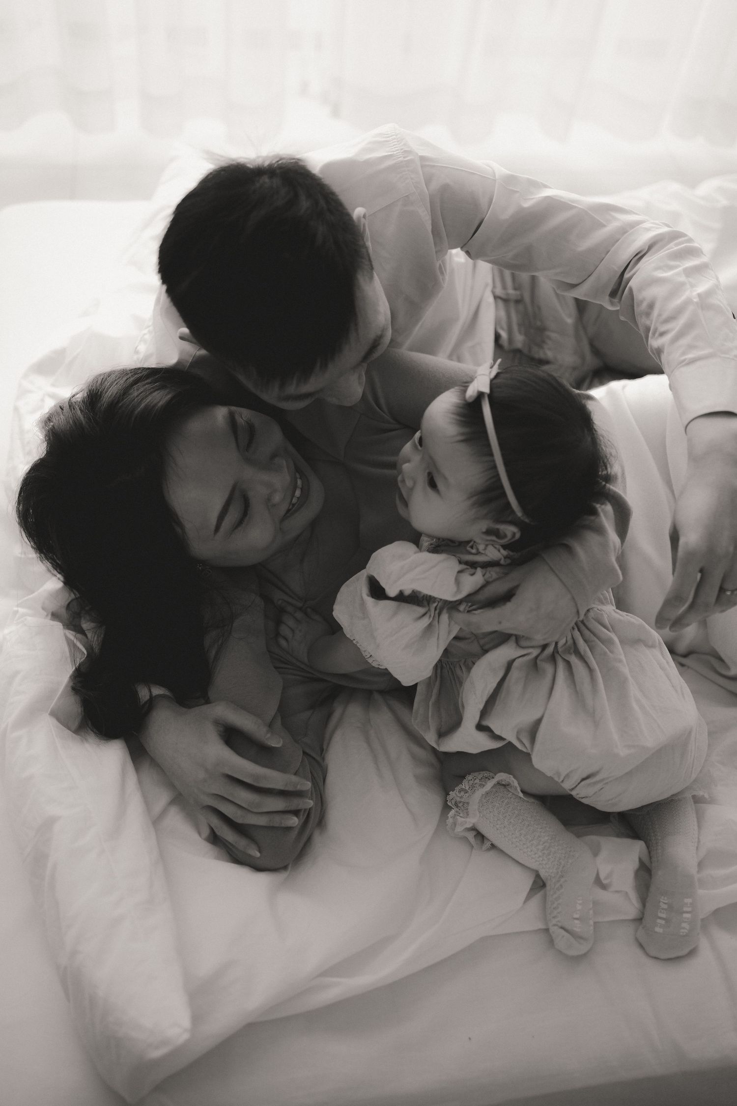 Black and white photo of a loving family with parents and baby cuddling together on a bed.一張黑白照片，照片中一個溫馨的家庭，父母和嬰兒依偎在床上。