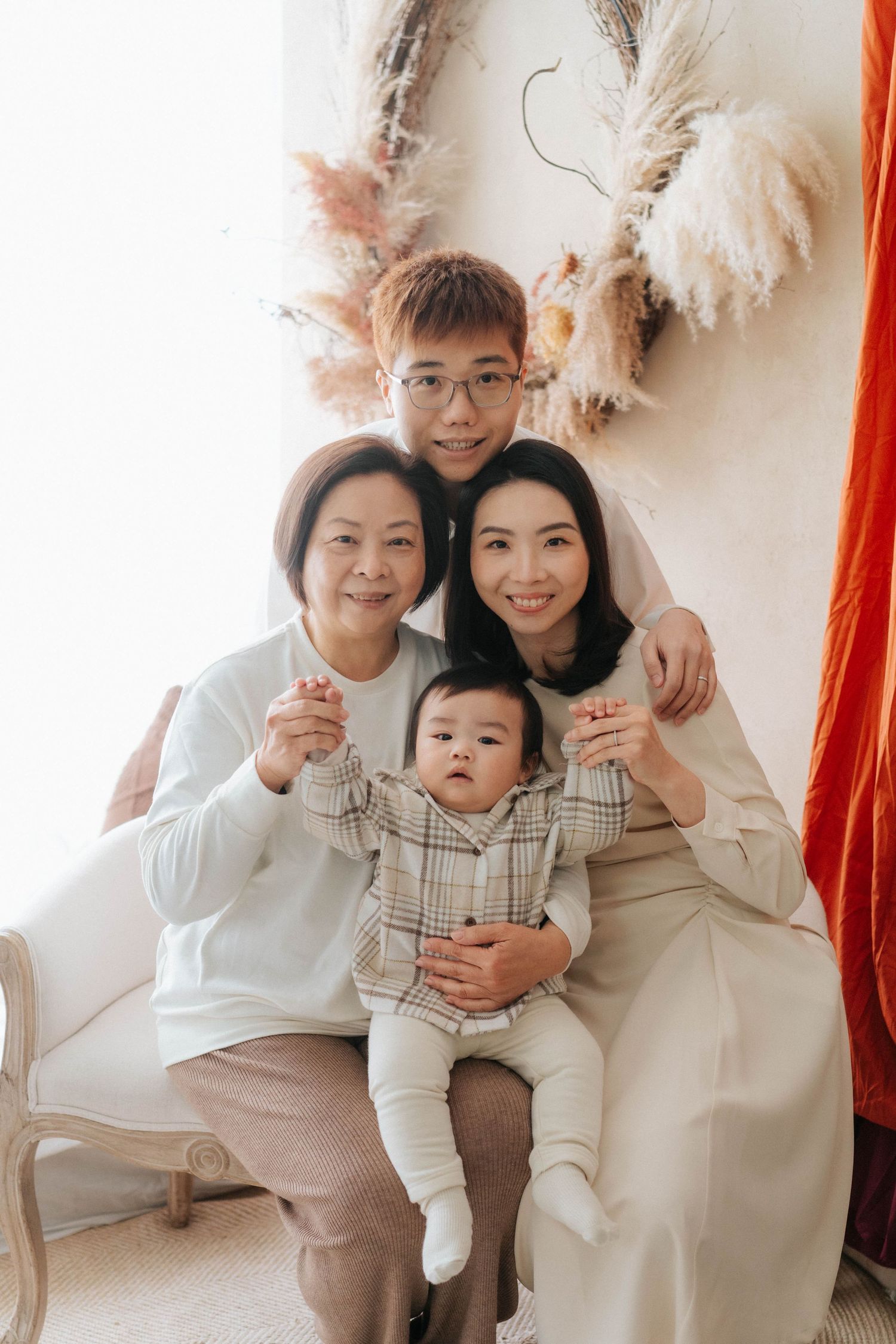 Multi-generational Asian family portrait with grandmother, parents, and baby posing together in a bright, cozy studio setting.一張亞洲多代家庭合影