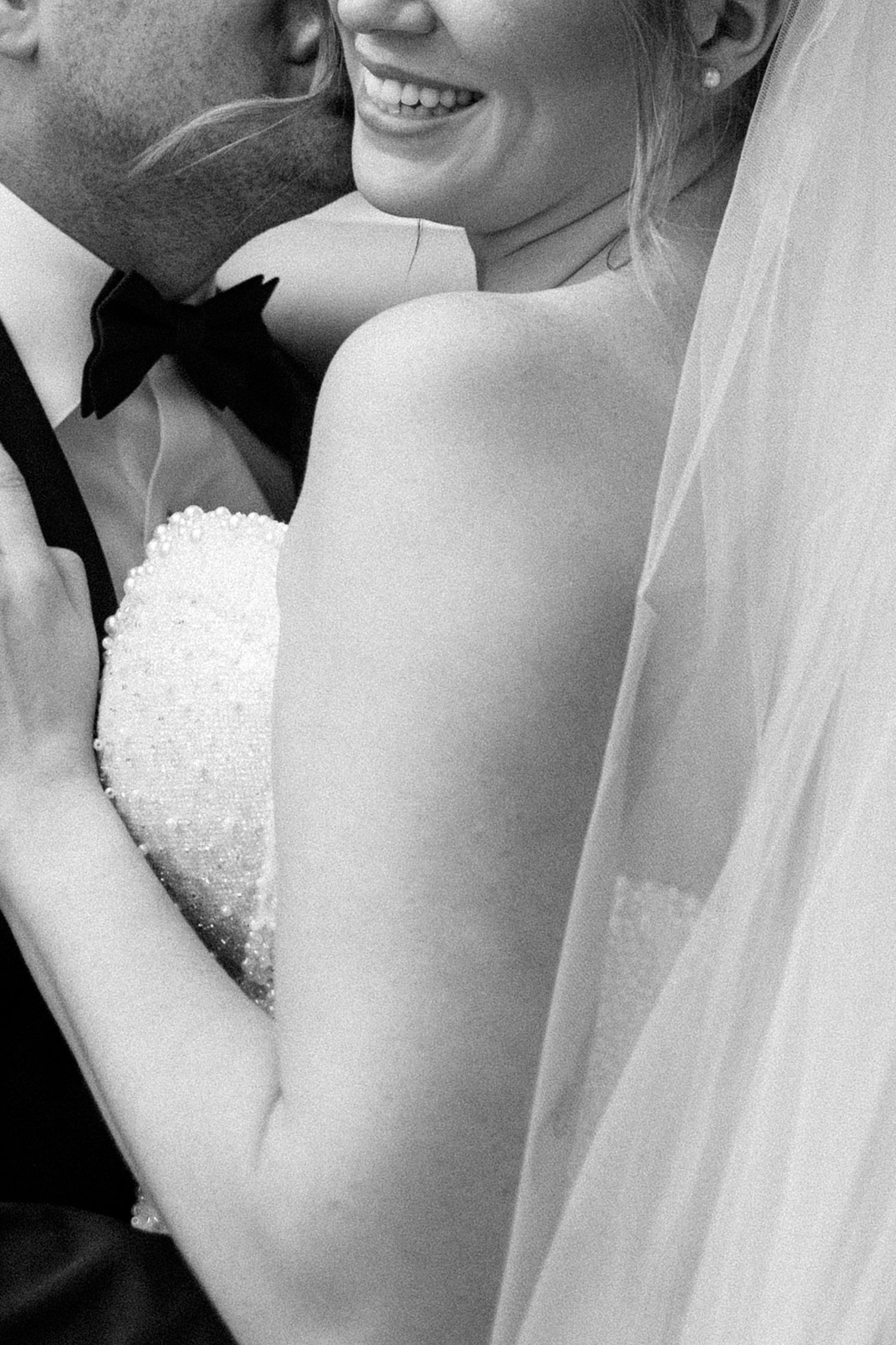 Black and white wedding photo showing intimate close-up of newlyweds embracing and smiling together.