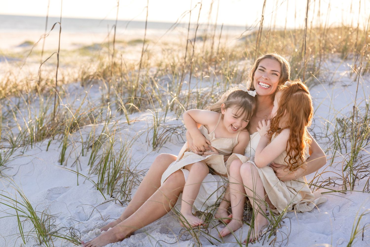 A group sits together on white sand dunes at sunset with beach grass swaying in the golden light.