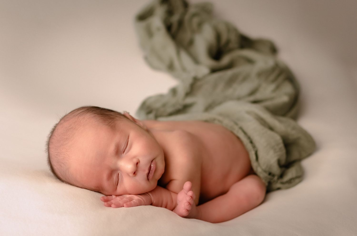 A sleeping newborn baby lying on soft beige fabric in a peaceful pose.