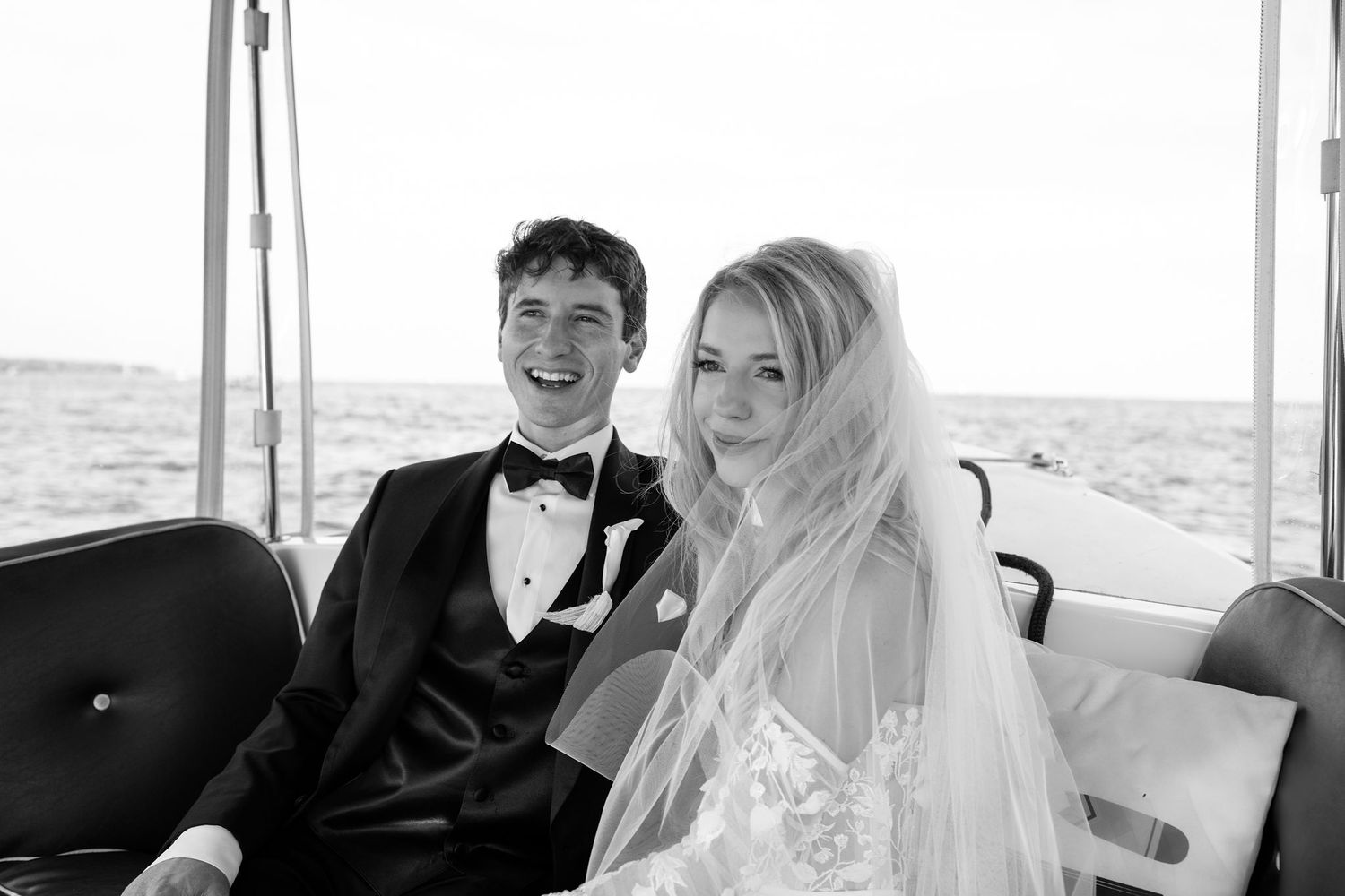 A black and white photo of a newlywed couple sharing a joyful moment while riding in a vehicle together.