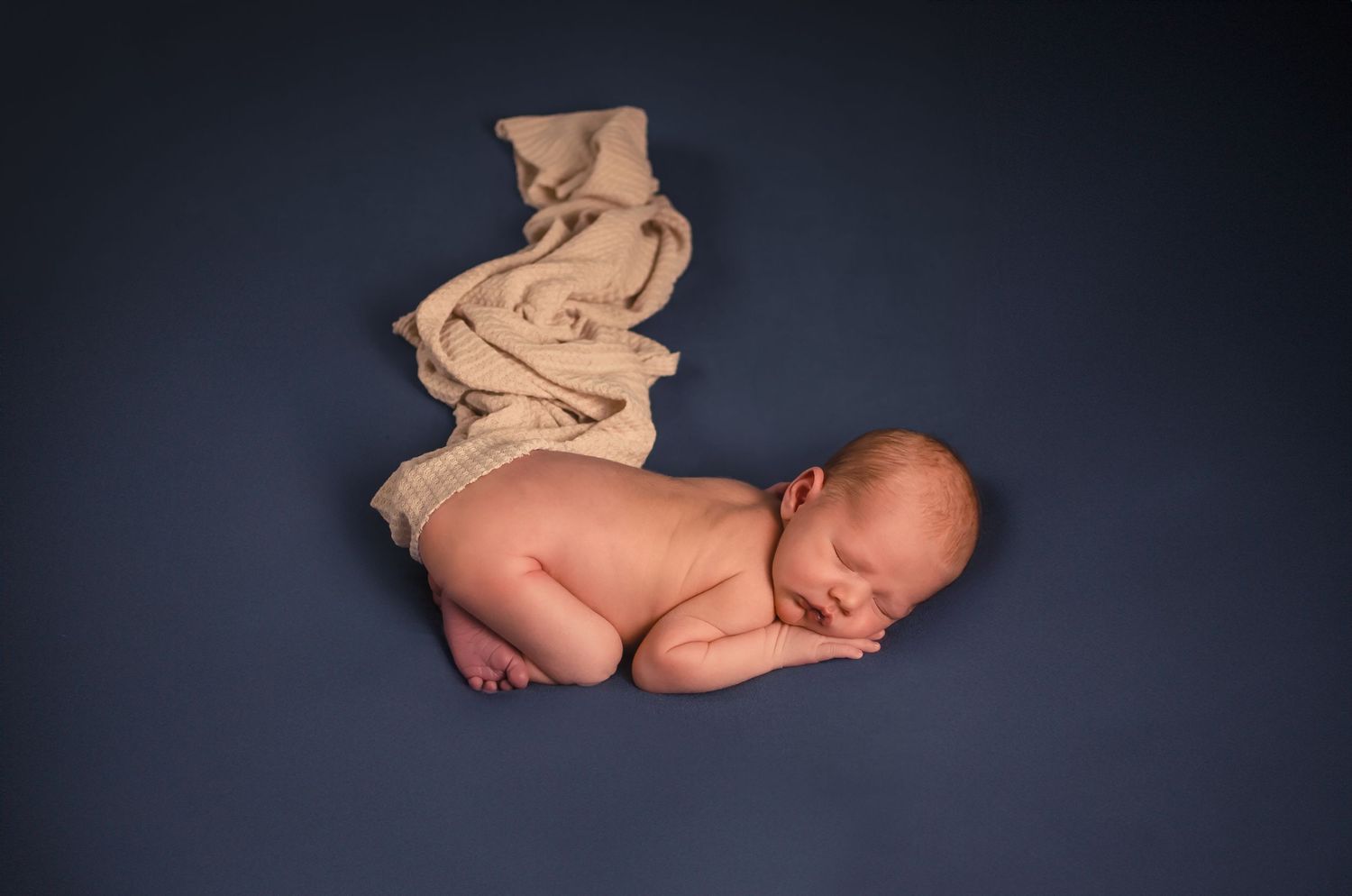 A sleeping newborn baby in a curled up pose against a dark background.