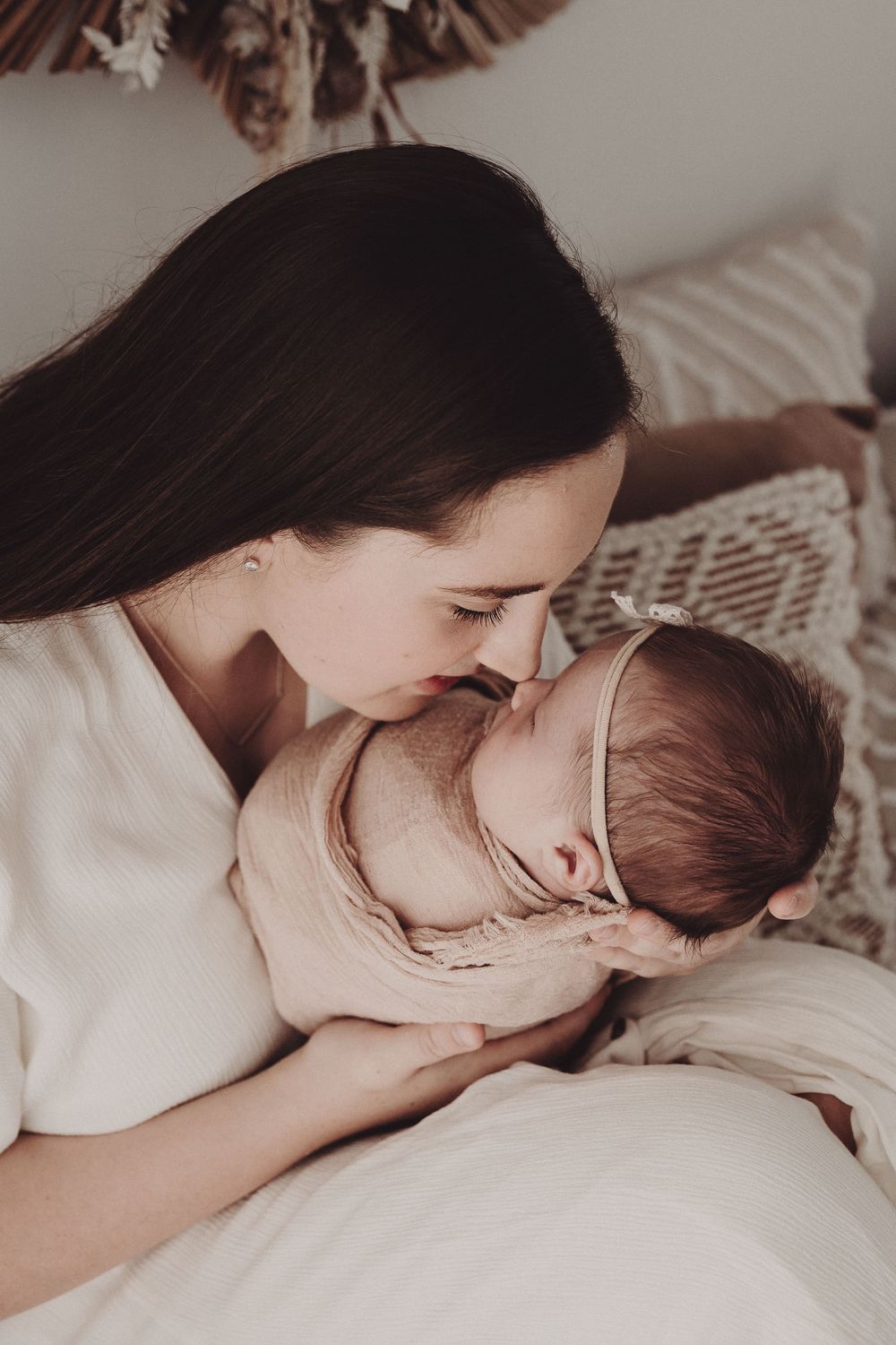 A tender moment captured in sepia tones showing nurturing care and affection between parent and infant on white bedding.