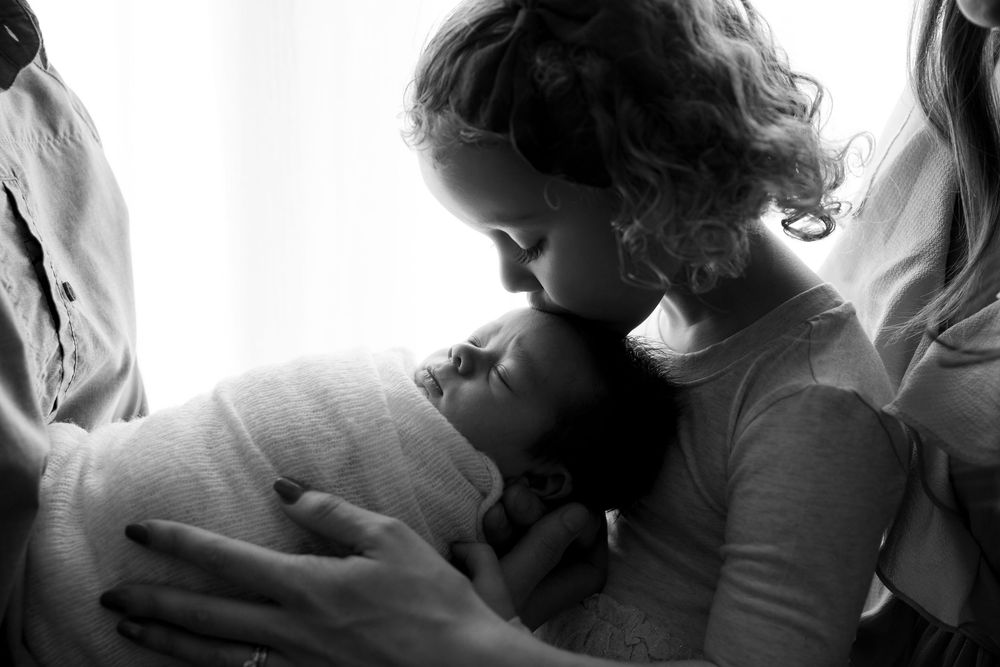 A tender black and white photograph showing a parent gently cradling and kissing a newborn baby.