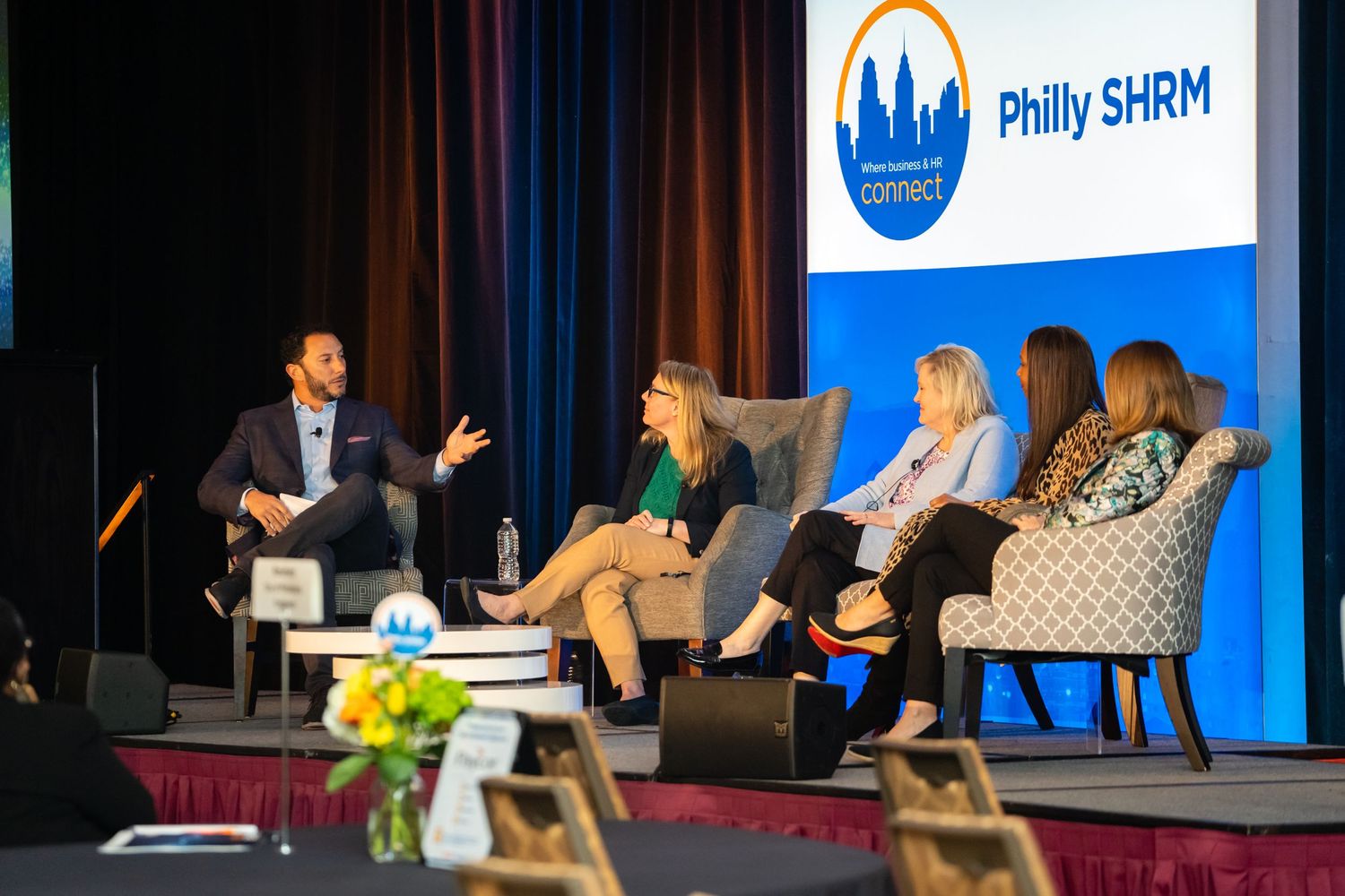 Professional speakers engage with audience during business conference presentation on stage with blue backdrop.