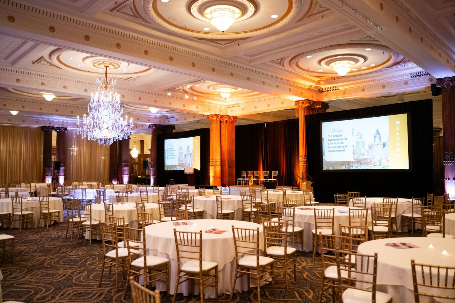 Elegant ballroom with crystal chandeliers, white chiavari chairs, and ornate ceiling details creates a luxurious event space.