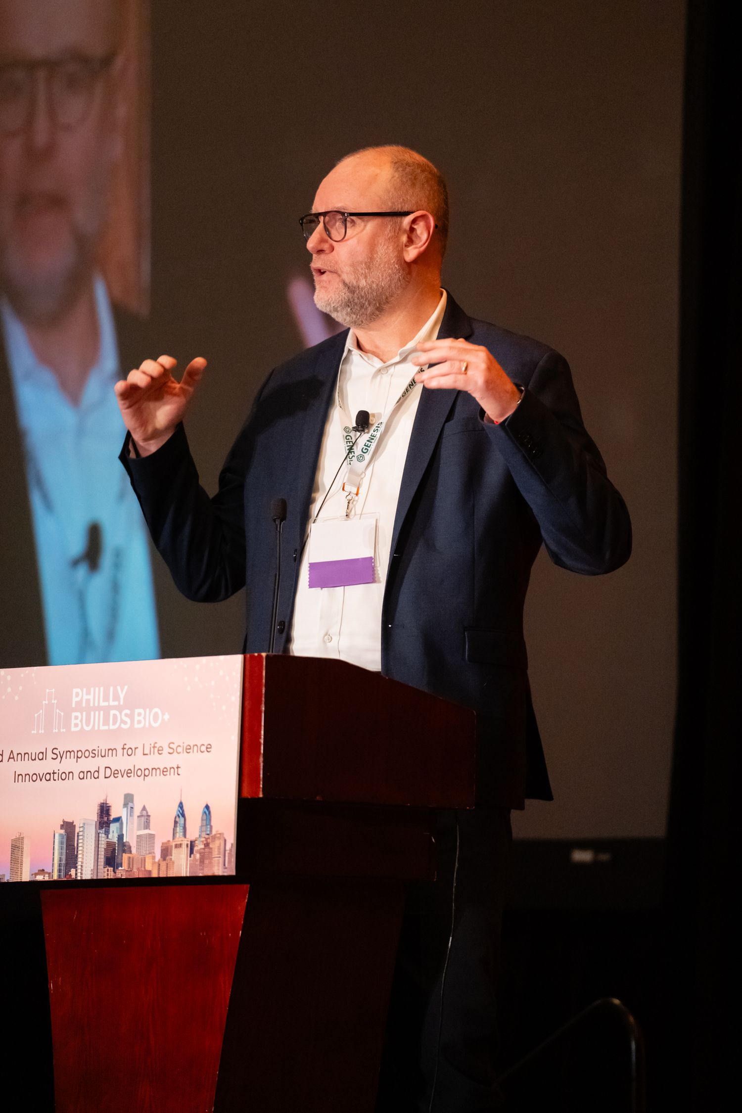 Business presenter in dark suit gestures while giving animated speech at conference podium.