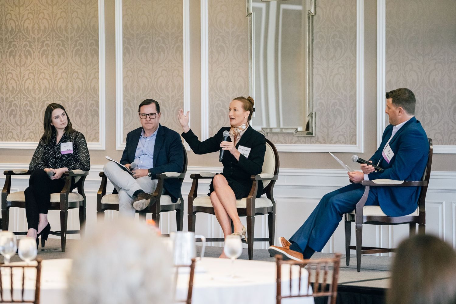 Business professionals participate in a panel discussion while seated on chairs in a conference room.