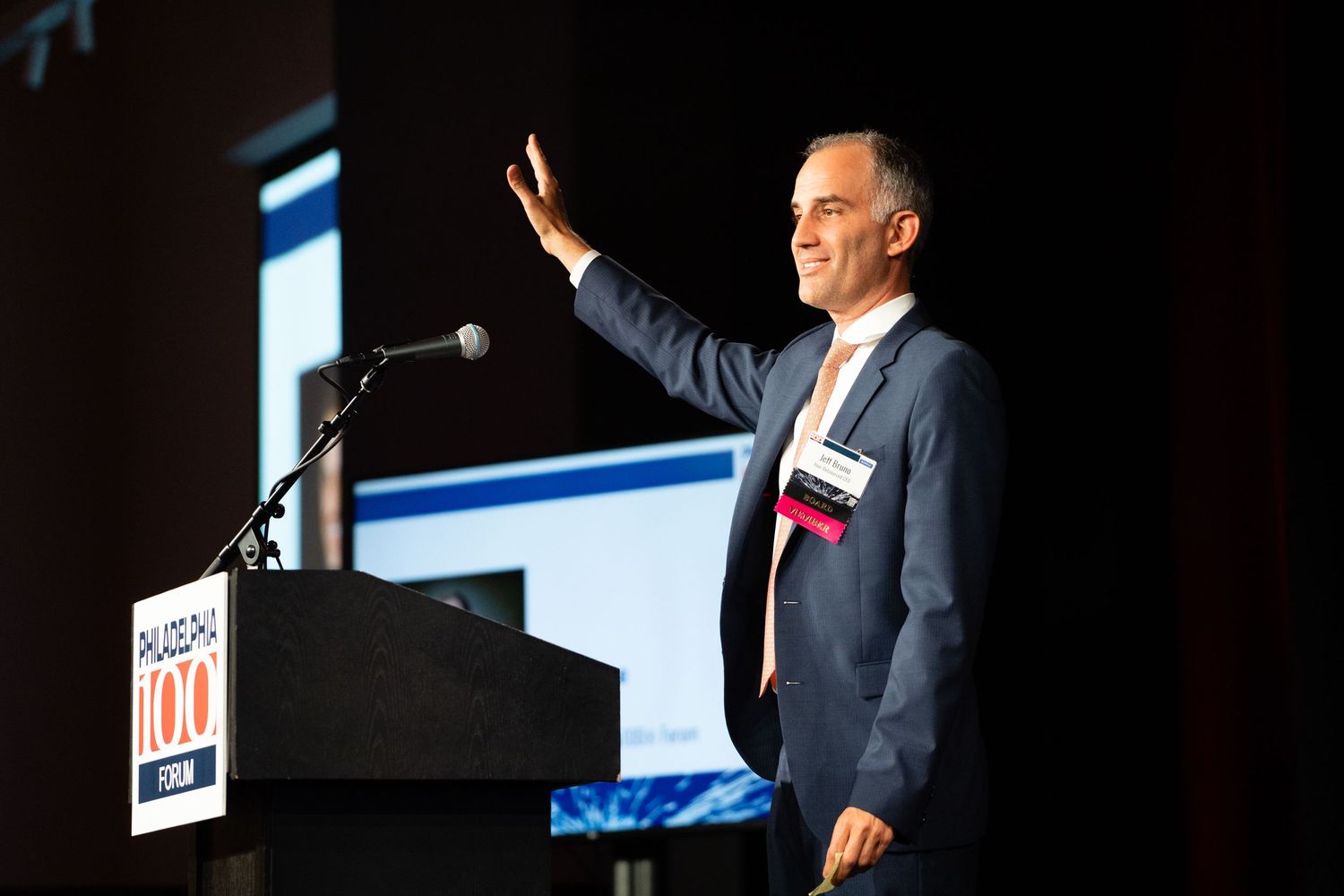 A speaker gestures while giving a presentation at a podium during a professional conference event.