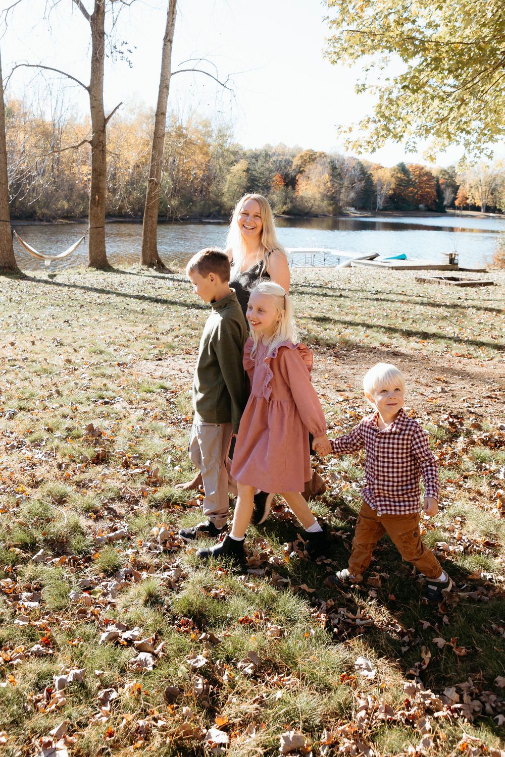 Family enjoying an autumn day together on a grassy slope near a lake with fallen leaves. Candid fun moments of mother and children walking.