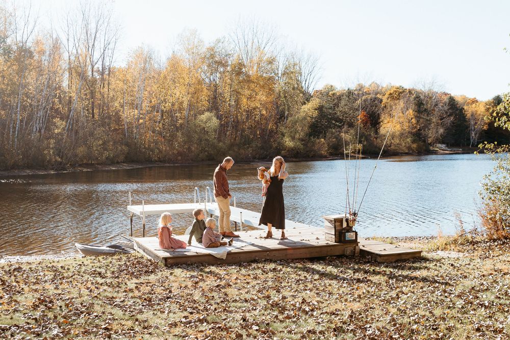 Group walking along a scenic lakeside path covered in fallen autumn leaves. Fall family lakeside photo session. Lake in  Michigan.