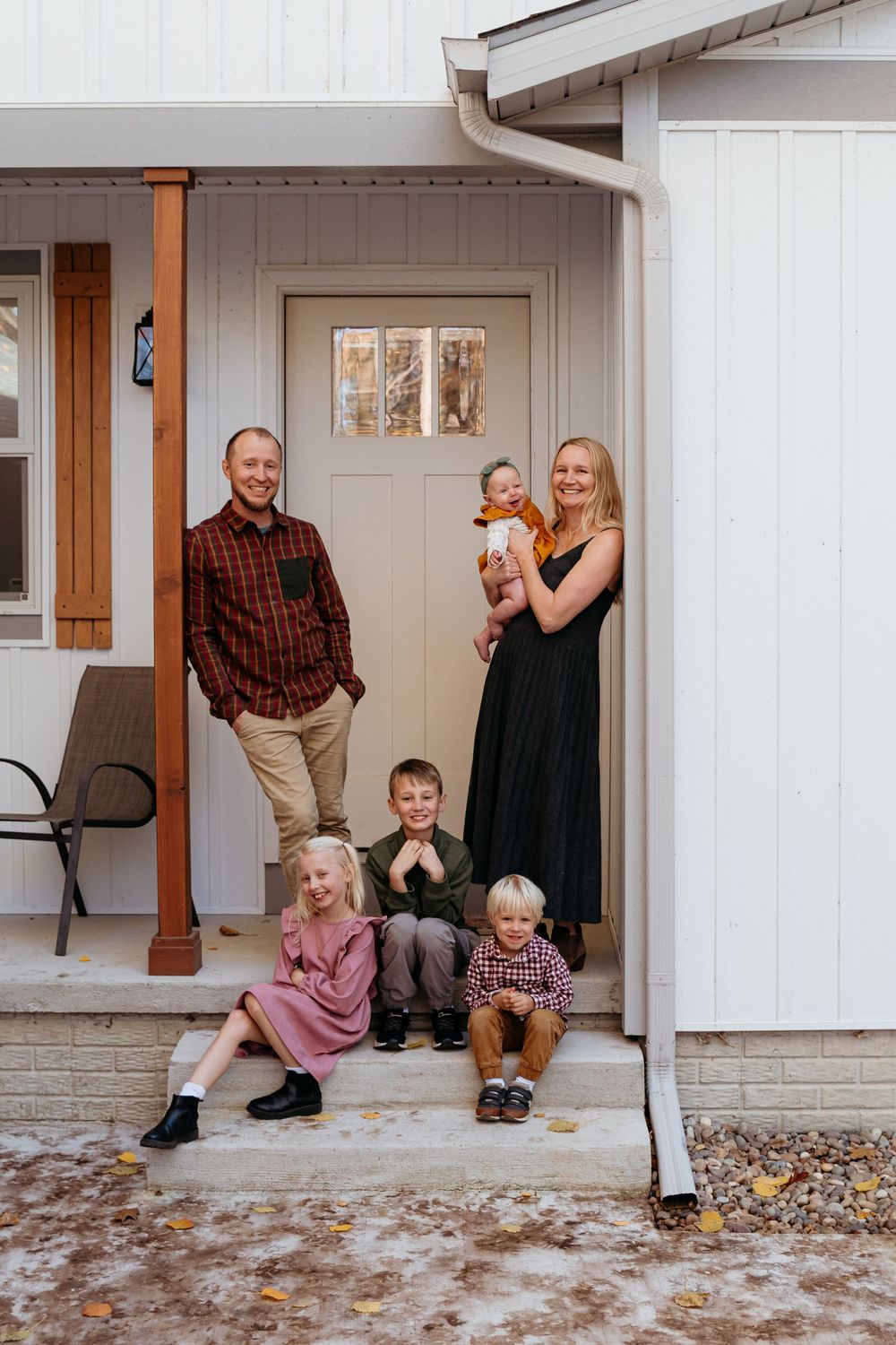 Family posing together on their front porch steps of a white house. Central Michigan family photographer.