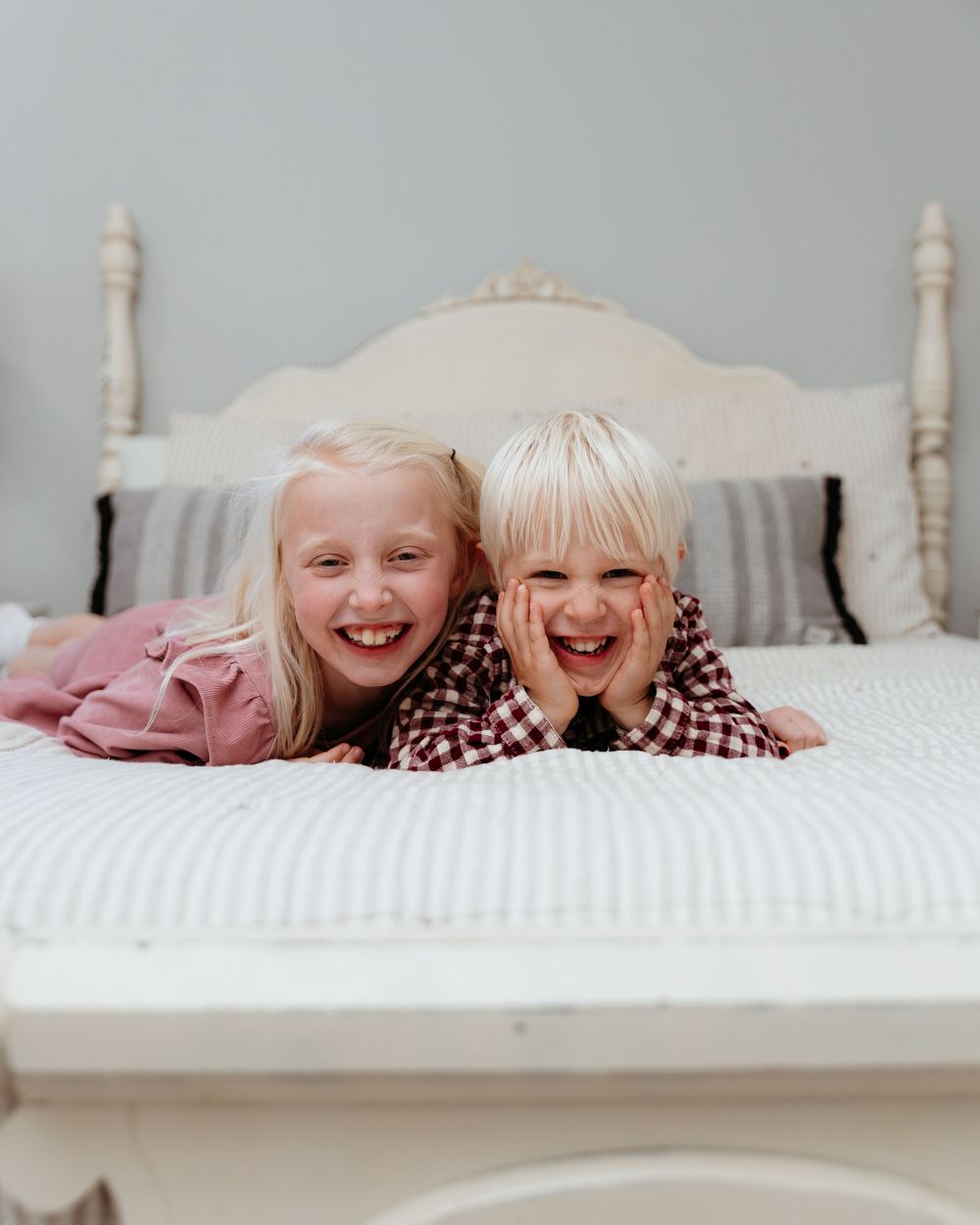 Two people lying together on a white bed sharing joyful laughter. Family portraits in-home photo session. Michigan family photographer.
