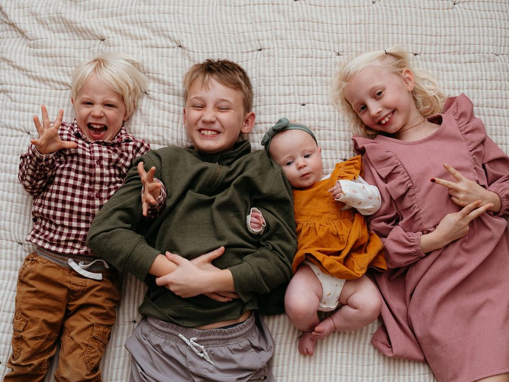 Family members lying together on a blanket sharing laughs and embraces. Children laughing at in-home bedroom session.