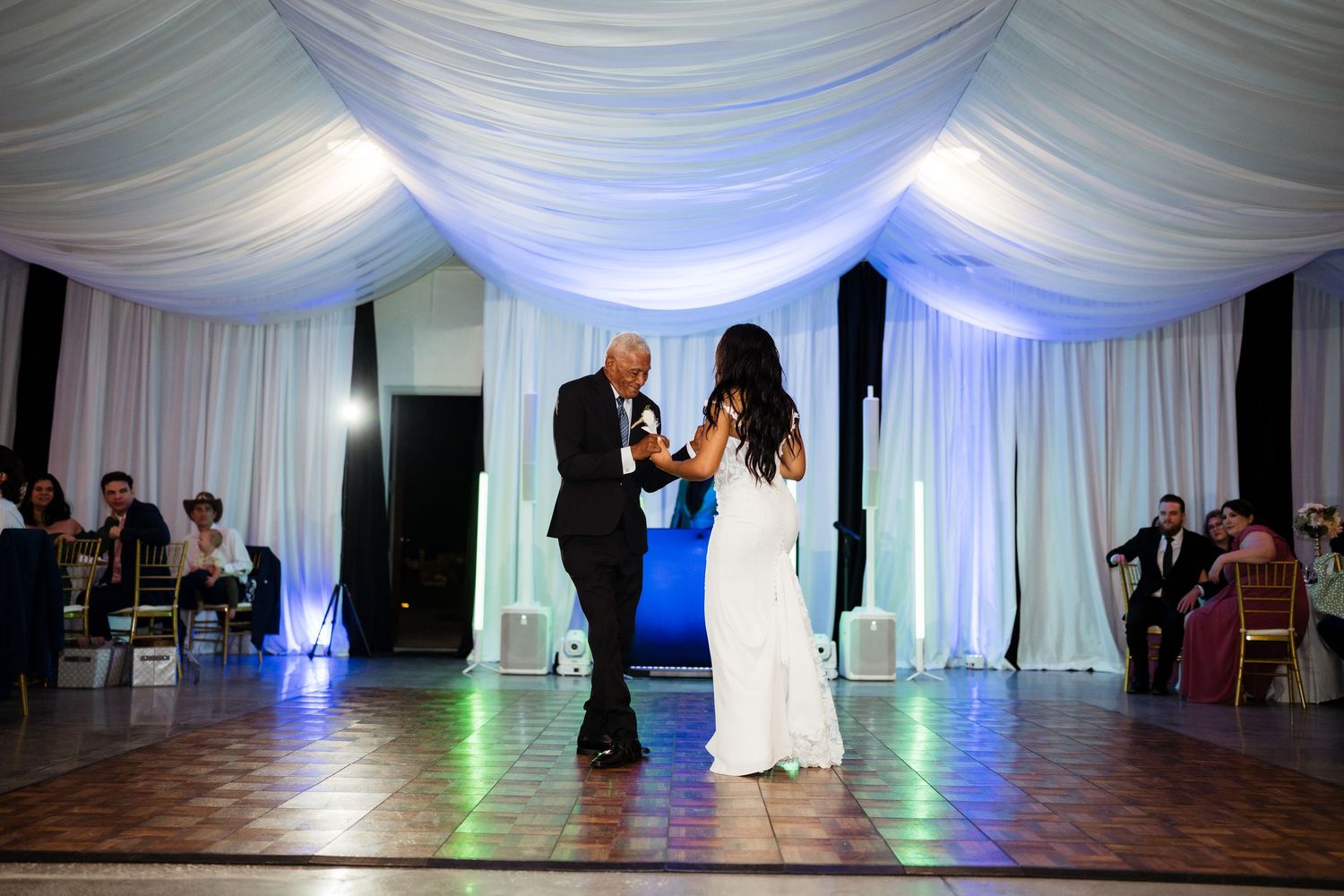 Wedding reception dance floor with white draping and blue uplighting creates an elegant atmosphere for celebration.