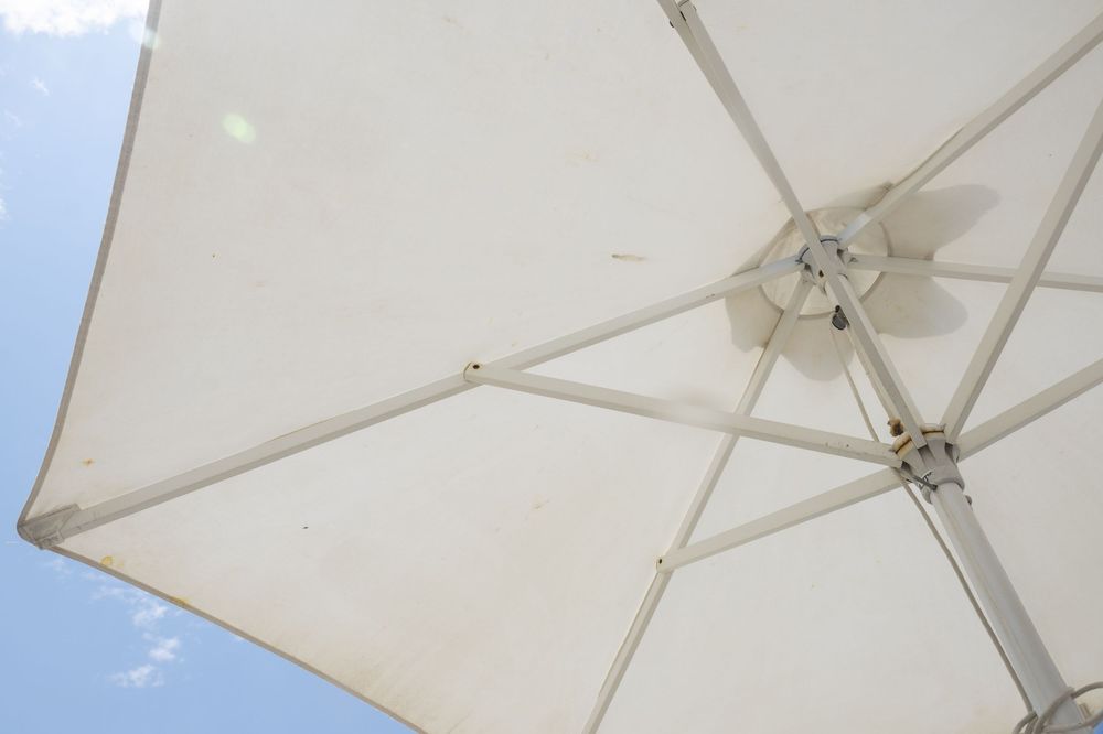 White patio umbrellas provide shade over an outdoor seating area on a bright sunny day.