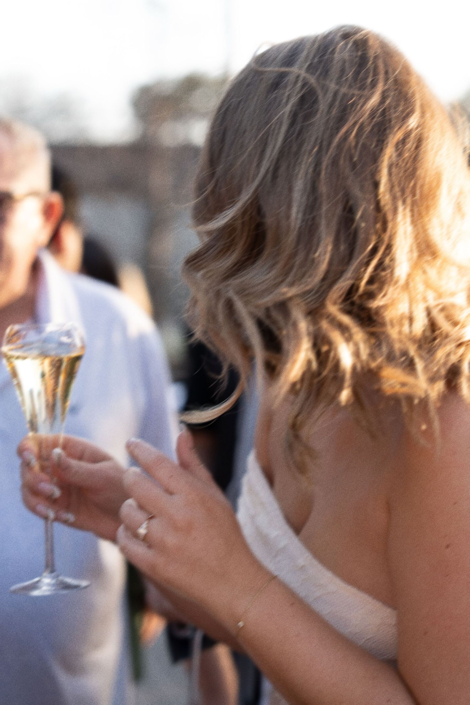 Wedding guests holding champagne glasses during outdoor celebration at sunset.