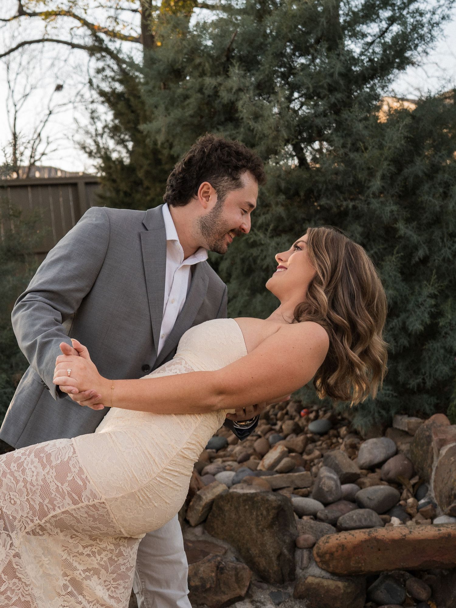 Romantic couple embracing and laughing in garden setting during sunset photoshoot.