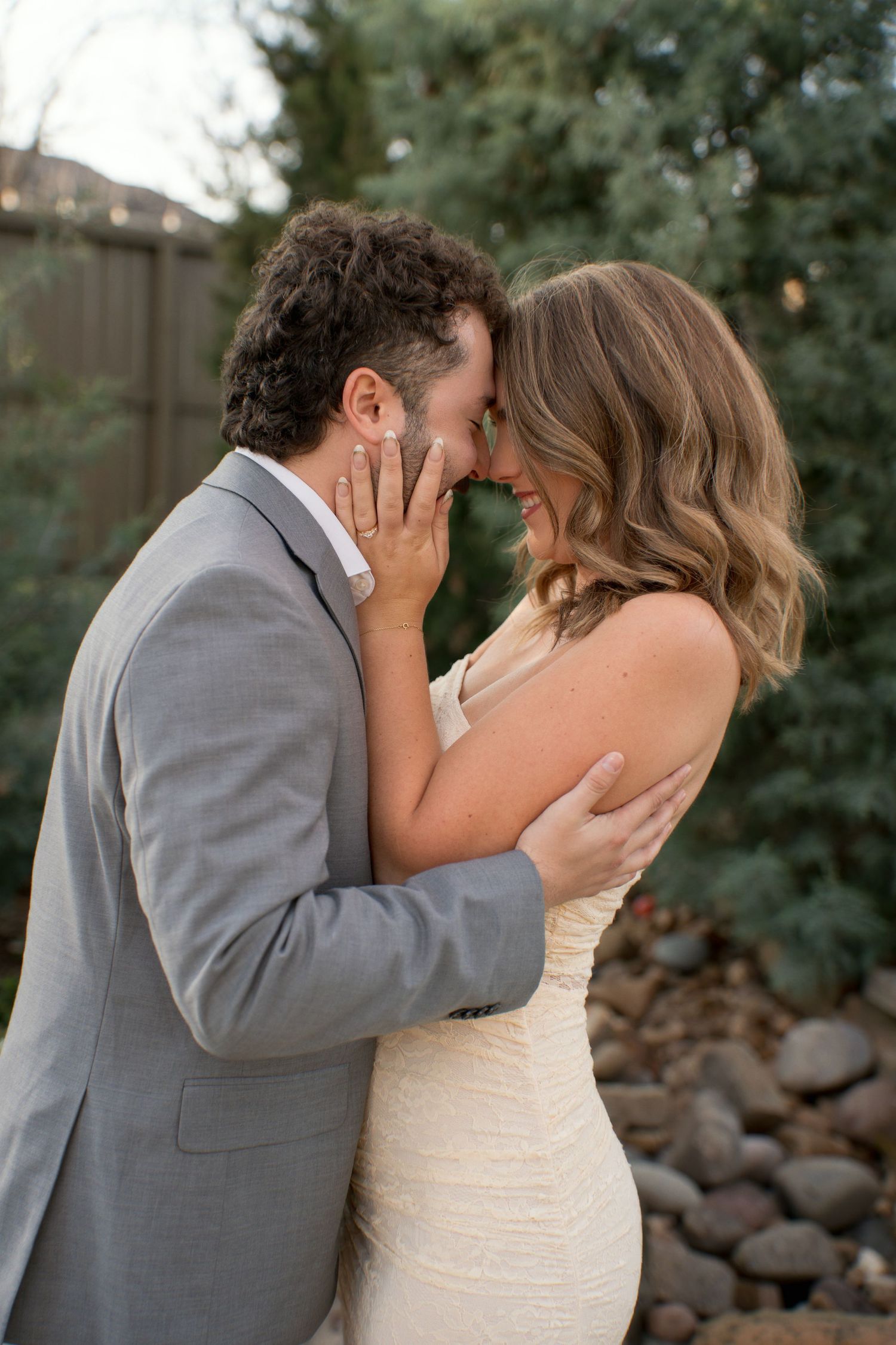 Intimate wedding moment captured outdoors with grey suit and white dress details.