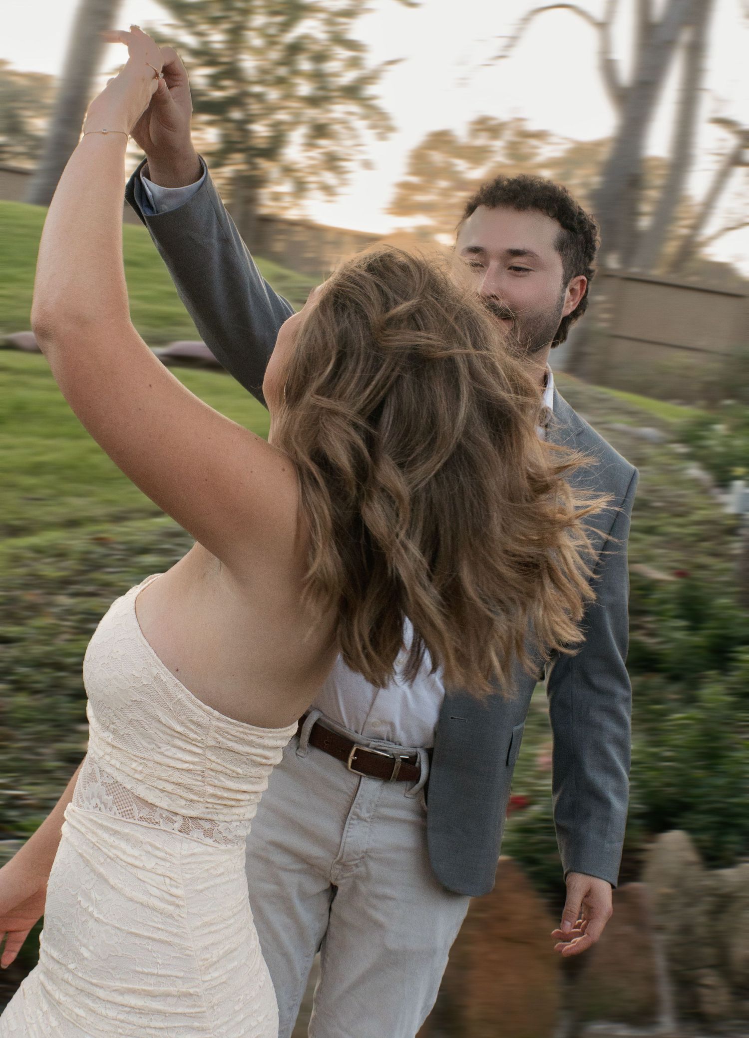 A couple dancing together outdoors with the bride wearing a white dress and groom in grey attire.