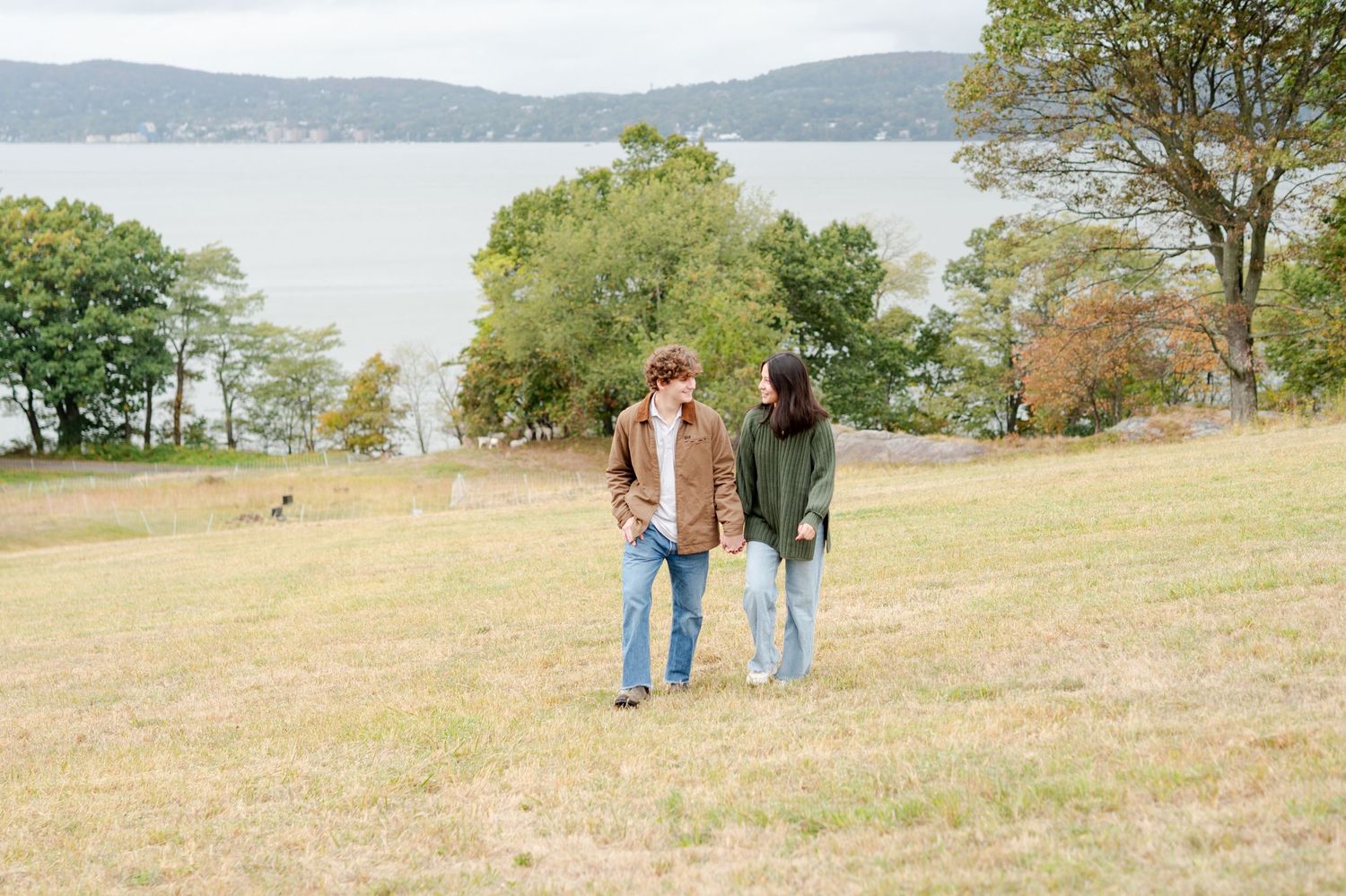 Two people walking together on a grassy hillside overlooking a tranquil lake on an autumn day.