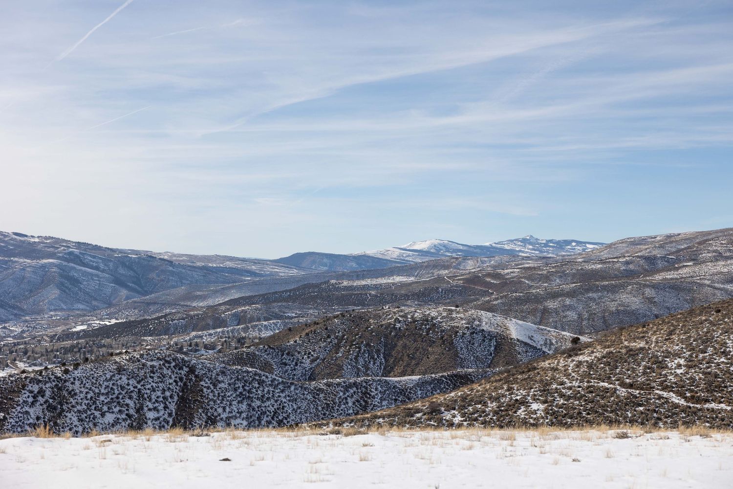 Panoramic winter landscape of snow-covered mountains and rolling hills stretching across the horizon.