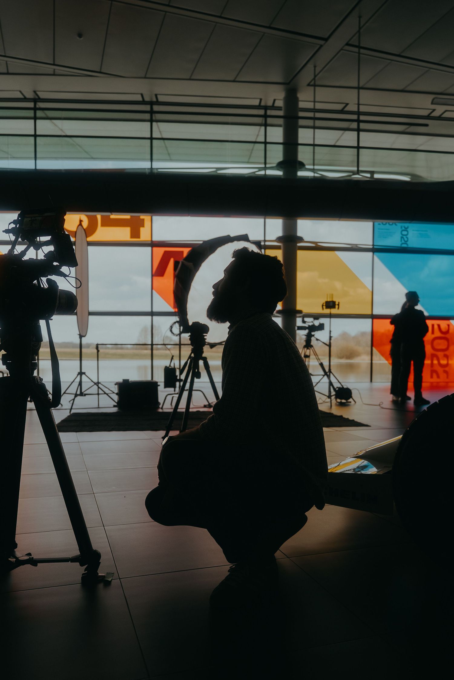 Silhouetted figures work with camera equipment in a studio with colorful backdrop panels and lighting setup.