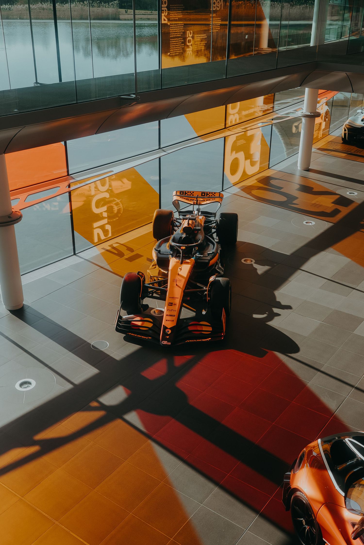 Formula 1 racing car on display in a modern showroom with orange and red lighting effects on the floor.